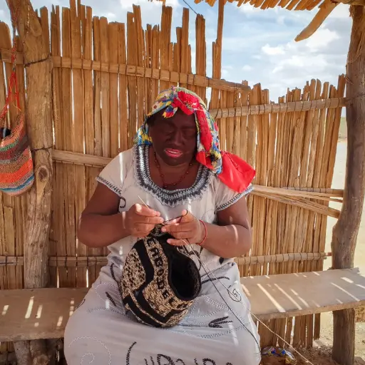 Wayuu-lady-sitting-on-a-bench-weaving-a-Wayuu-bag-known-as-a-Mochila